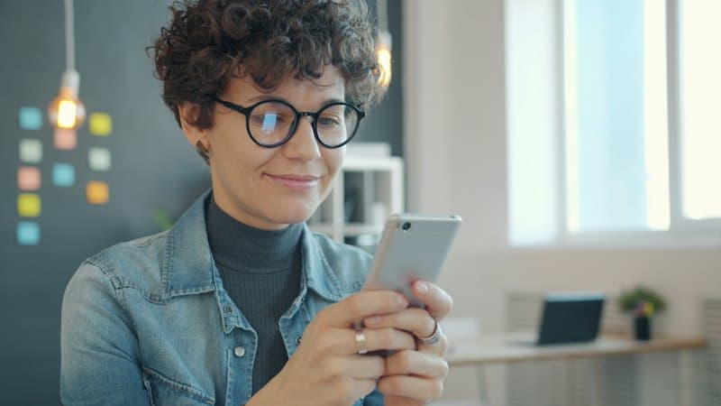 Mulher de óculos sorrindo enquanto usa o celular