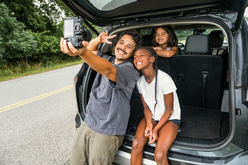 Família tirando uma selfie no porta-malas aberto do carro, na beira da estrada