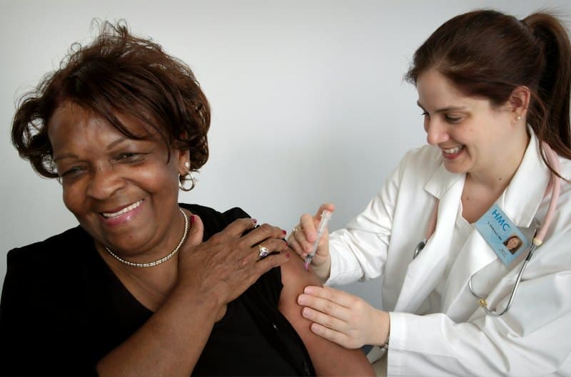 Médica aplicando vacina no braço de uma senhora sorridente